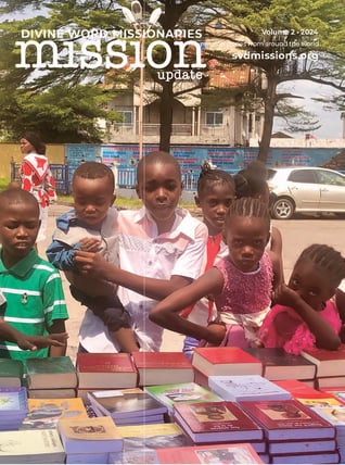 Children stand around a table with books at an outdoor event. The words "Divine Word Missionaries Mission Update" are at the top.